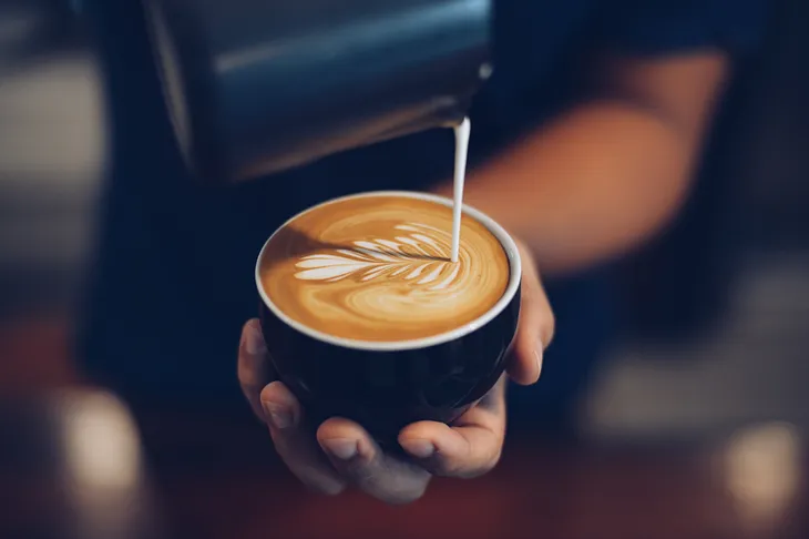 A close-up of a barista pouring milk to create a leaf pattern on an espresso base.