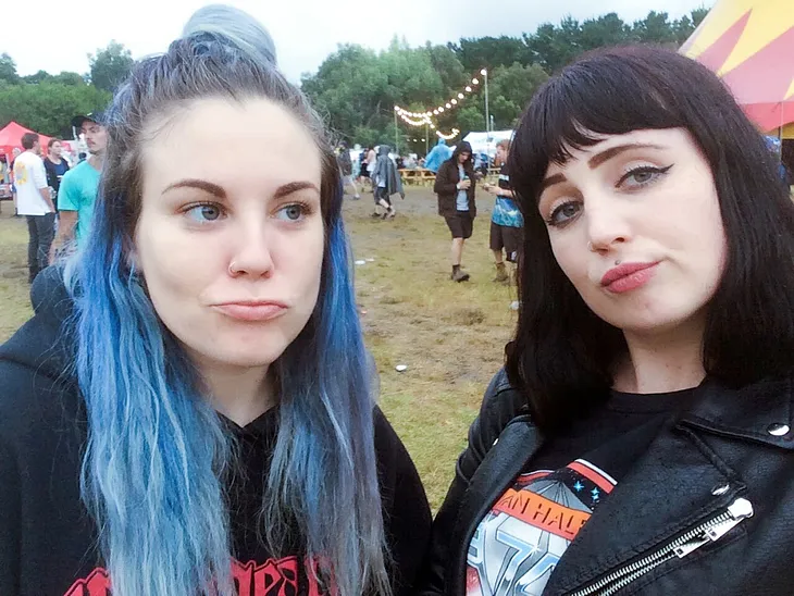 Two young women at an outdoors music festival with unimpressed facial expressions