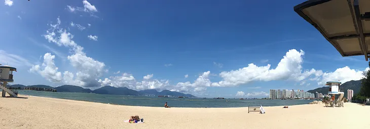 A panorama view of a beach of sunny blue sky with super white clouds on the yellow sand.