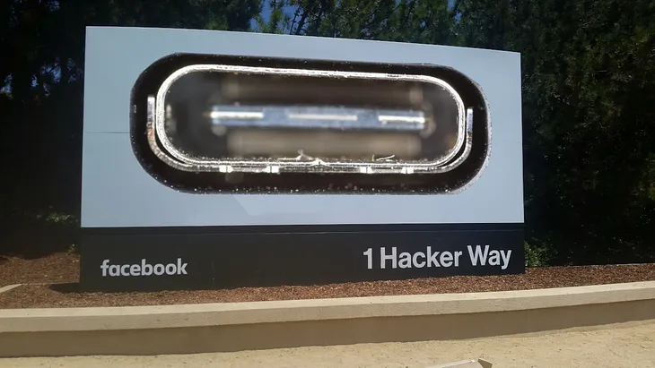 Facebook HQ’s iconic ‘1 Hacker Way’ sign. The Facebook logo has been replaced with a giant USB C port. Image: D-Kuru (modified) https://commons.wikimedia.org/wiki/File:MSI_Bravo_17_(0017FK-007)-USB-C_port_large_PNr%C2%B00761.jpg Minette Lontsie (modified) https://commons.wikimedia.org/wiki/File:Facebook_Headquarters.jpg CC BY-SA 4.0 https://creativecommons.org/licenses/by-sa/4.0/deed.en