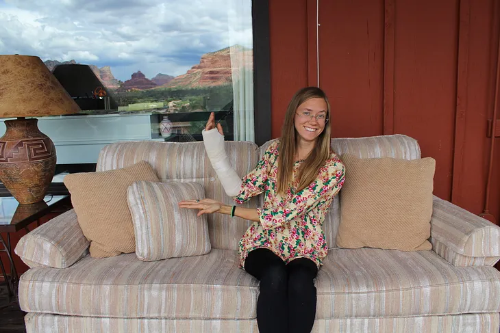 A young woman sitting on a couch holding up an arm in a cast