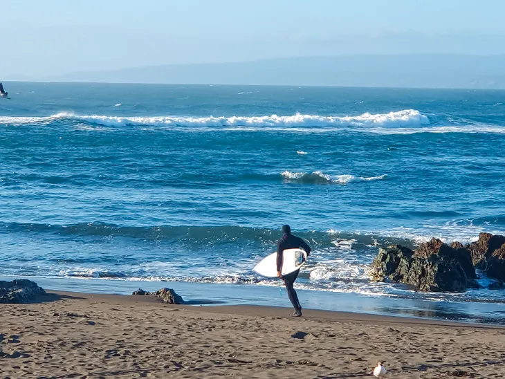 surfer in wetsuit running along the beach in Pichilemu Chile, holding a surfboard