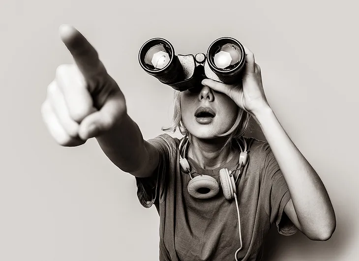 Woman using binoculars and pointing at the Kingdom of Heaven in the distance, where it isn’t.