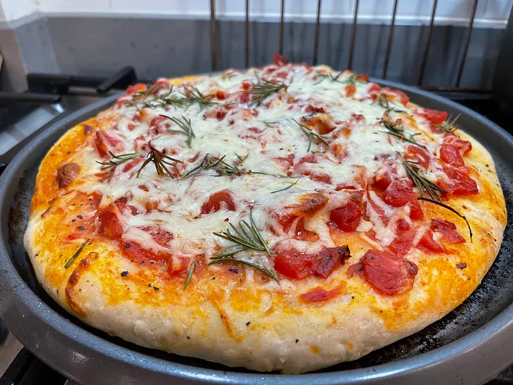 A large homemade pizza with tomatoes, mozarella cheese, and rosemary