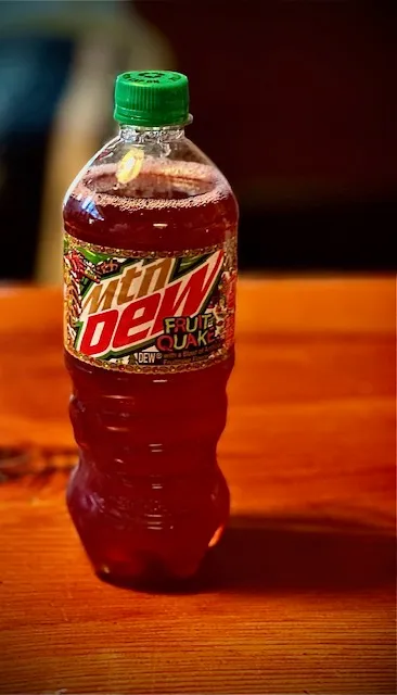 Picture of a bottle with reddish brownish rust colored liquid sitting on a wood table.