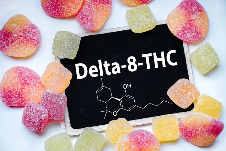 Chalkboard reading “Delta-8-THC” with a diagram of the chemical compound surrounded by yellow, orange, red and light green gummies