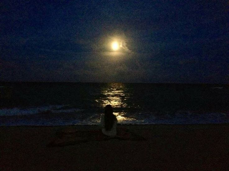 A person sitting under the moonlight, hands over their heart in a gesture of self-love