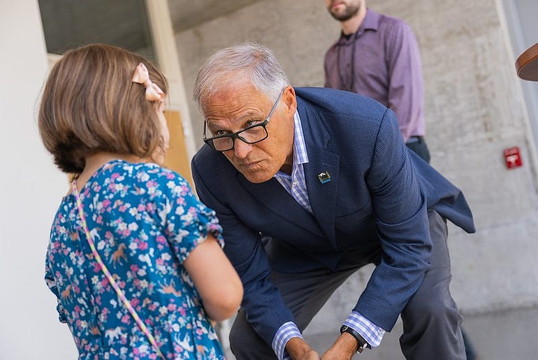 Gov. Inslee leaning down to greet a child in a floral dress