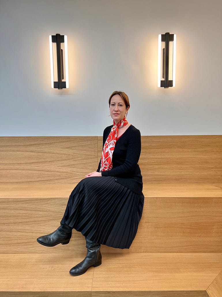 Photo of Allianz X CFO Catherine Dietrich sitting on a wooden bench, between two lights in an Allianz X meeting room