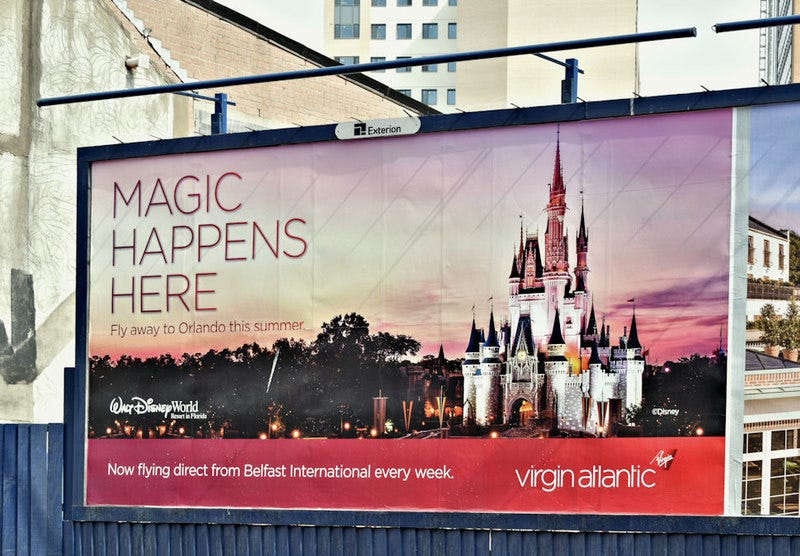 Like there’s no magic in Ireland! Marketers promote shared consumer rituals but at a deep ecological cost. (Image promoting flying to Disney World from Belfast from Albert Bridge via Geograph.ie)