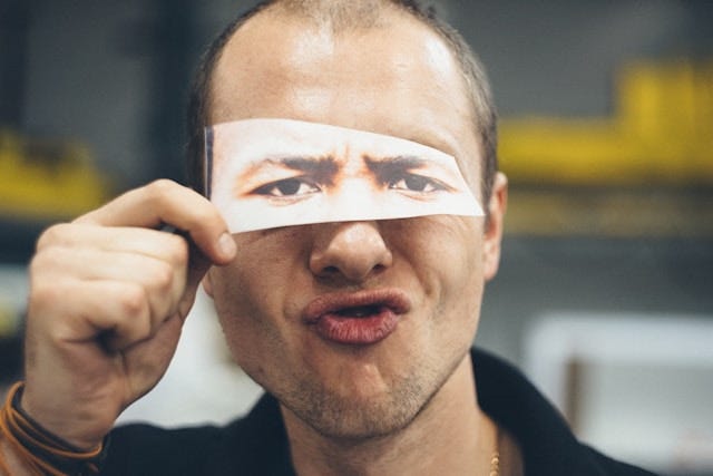 A man holds a paper with his face printed on it, symbolizing the rise of deepfakes and their impact on media and society.