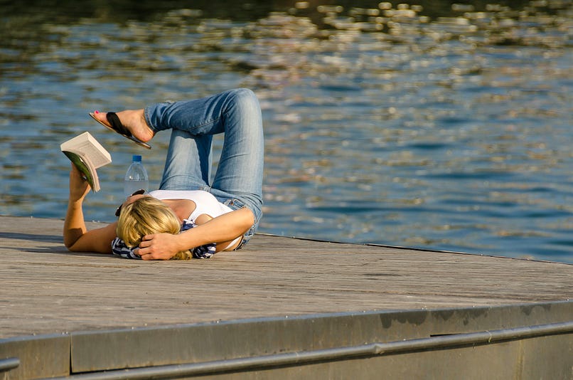 Woman reading a book on a pier.