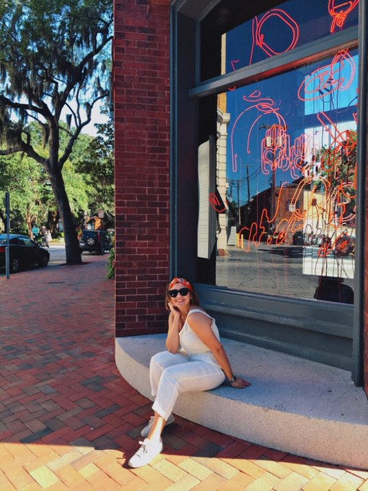 Deena sitting on step outside in front of store window.