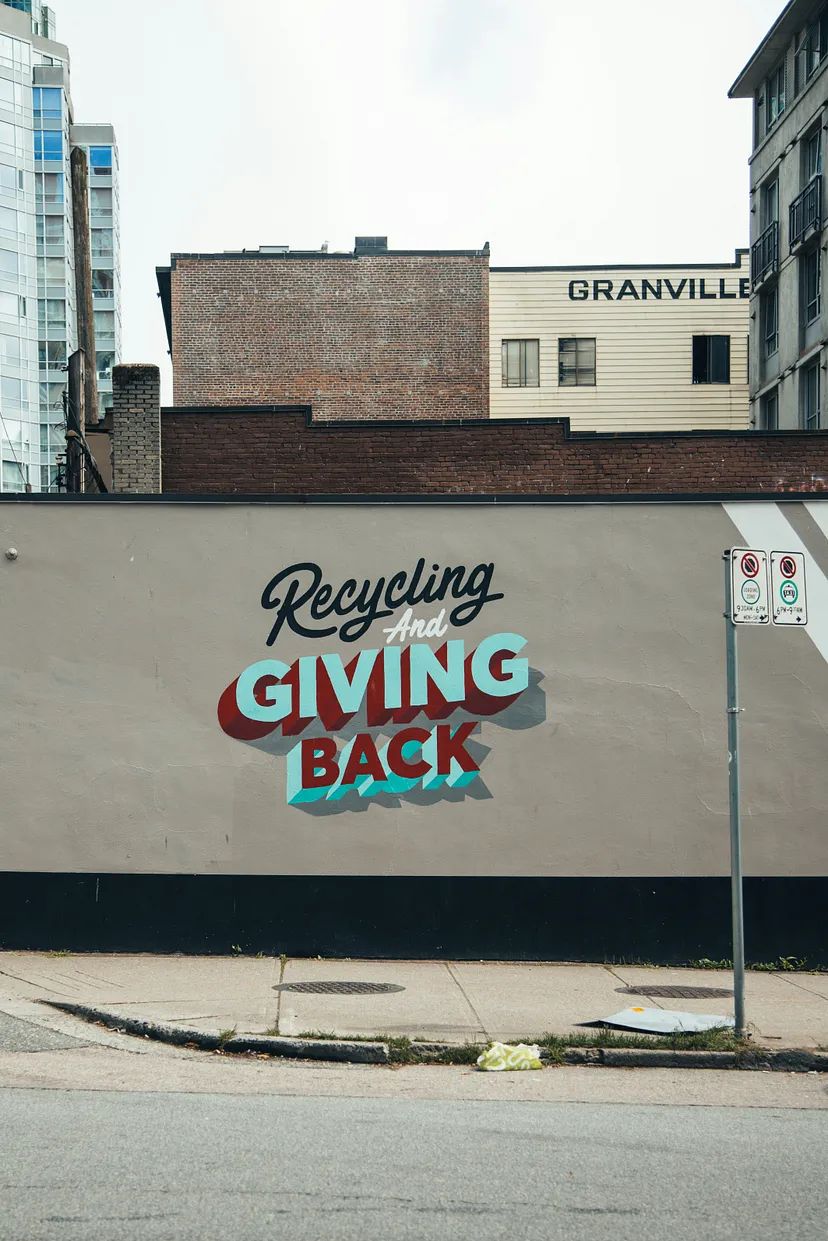 Sign on wall saying “Recycling And Giving Back” with buildings in the background Photo by Jack Church on Unsplash