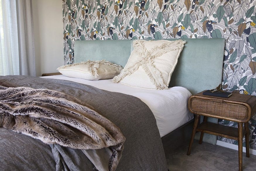 Une chambre principale magnifiquement décorée avec une tête de lit en velours sauge moelleux et un papier peint à imprimé feuillage