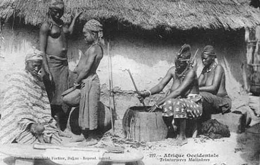 A black and white image of 5 African people, including 1 child, preparing indigo outside in 1905.