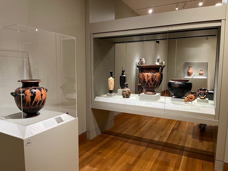 Installation image with orange and black colored vases in glass cases.