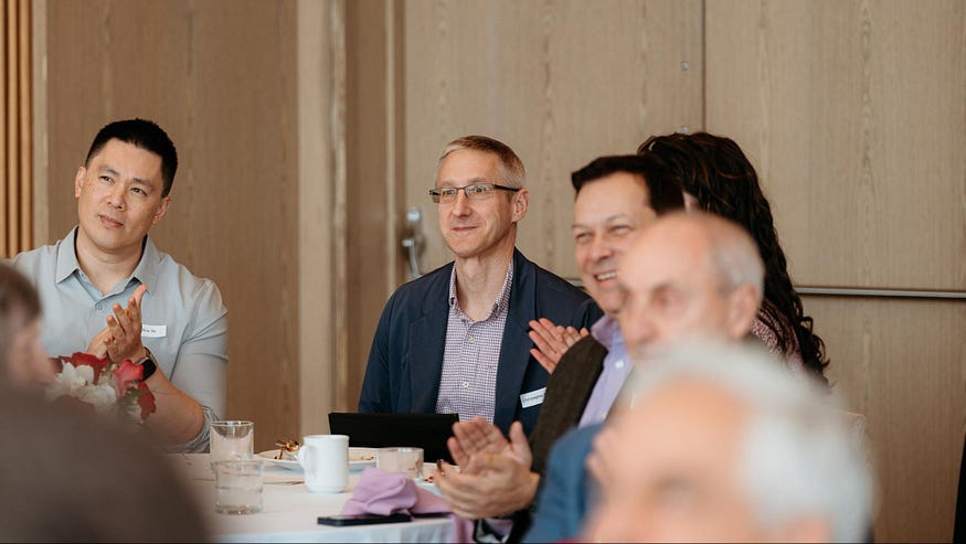 Colleagues clap in celebration of Christopher Noe, as they learn of the positive impact of his hands-on financial analysis.