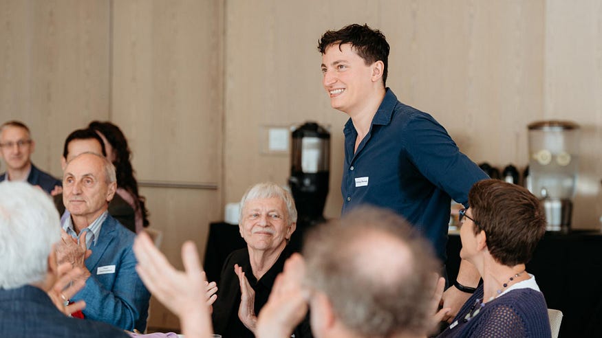Colleagues clap in celebration of Anthony Pennes, as they learn of how he inspires and instills confidence in student ideas.