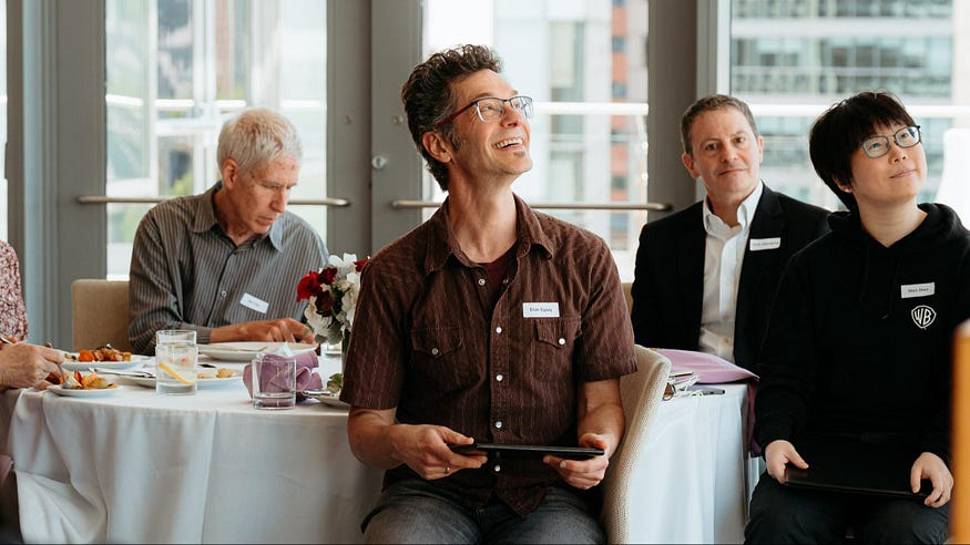 Eran Egozy smiling while holding his award certificate, as he listens to how his game demonstrations engaged students.