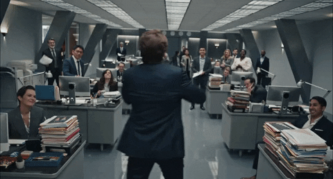 Man standing in a room full of people at their desk with records on their desk. Puts both hands out to the side to receive a standing ovation from the crowd. Caption says "You after you present at Share & Shine."