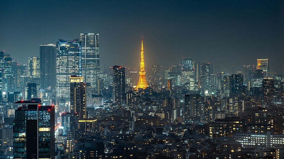 A high-angle night photograph of Tokyo, Japan. The Tokyo Tower is prominently illuminated in its traditional orange “Landmark Light.” To the left, several modern skyscrapers are visible, including the Azabudai Hills Mori JP Tower and the Roppongi Hills Mori Tower. Taken from the 35th floor of Shibuya Stream. Image from Wikimedia Commons