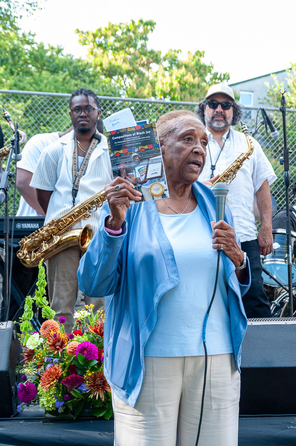 Johnson House Historic Site board president Pat Bass holds a copy of Compositions of Black Joy while addressing the audience gathered for the Jammin’ In The Garden fundraising event on September 20, 2025. Photographed by Tieshka Smith. This image is protected by copyright.